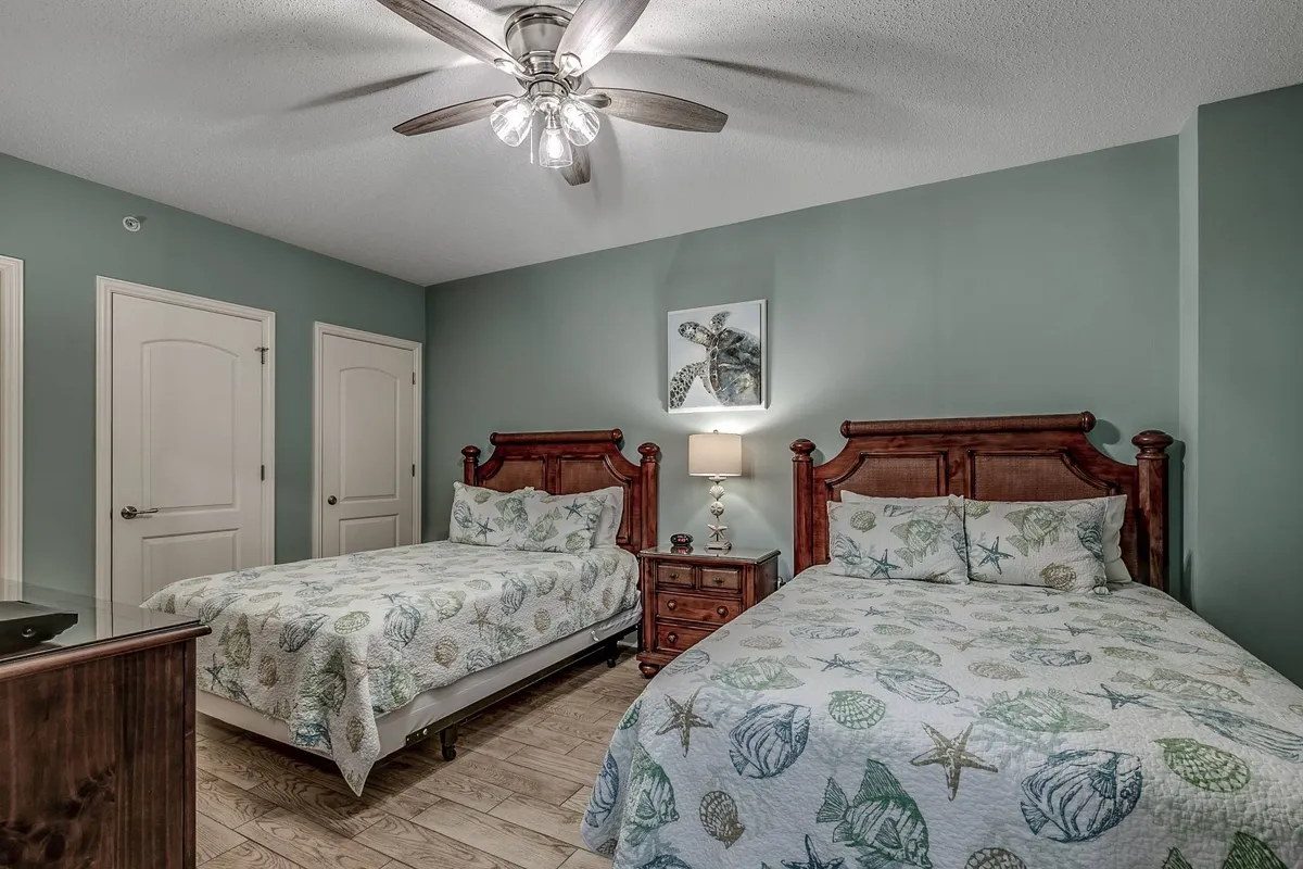 A guest bedroom with two queen beds adorned in decorative bedding, a cozy nightstand with lamp between them, and framed art above the beds. The space feels inviting, comfortable, and ideal for families or friends seeking flexibility.