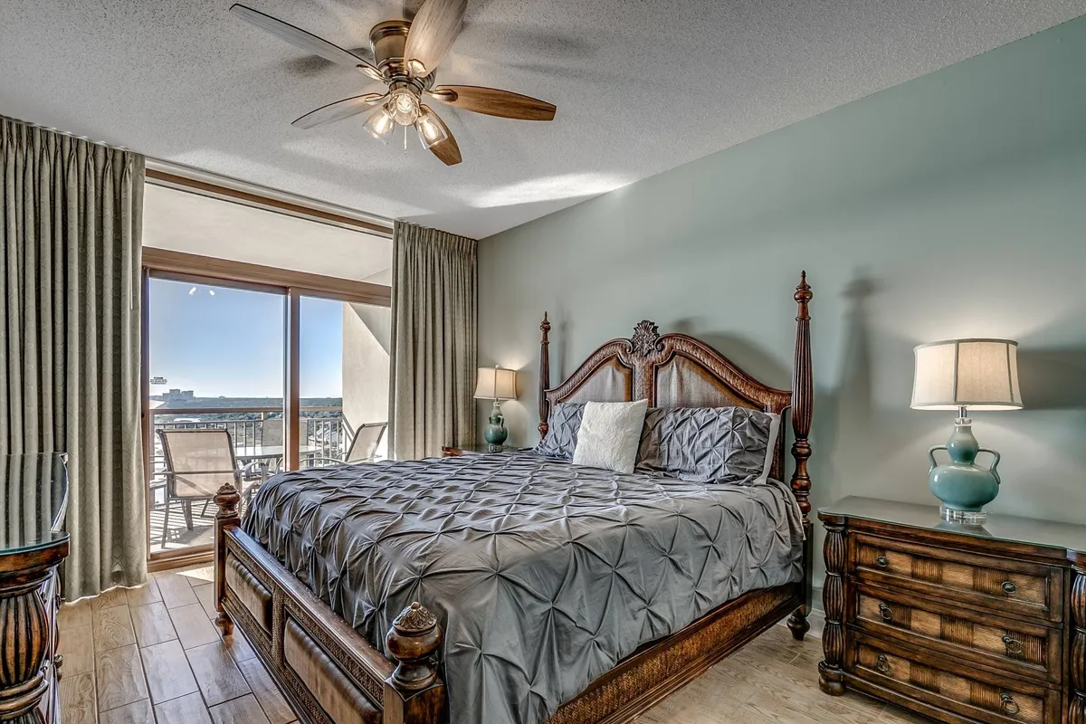 A serene master bedroom featuring a plush king-size bed with an ornate headboard, flanked by nightstands and lamps. Large windows offer abundant natural light and showcase a beautiful ocean view, creating a peaceful environment perfect for relaxation.