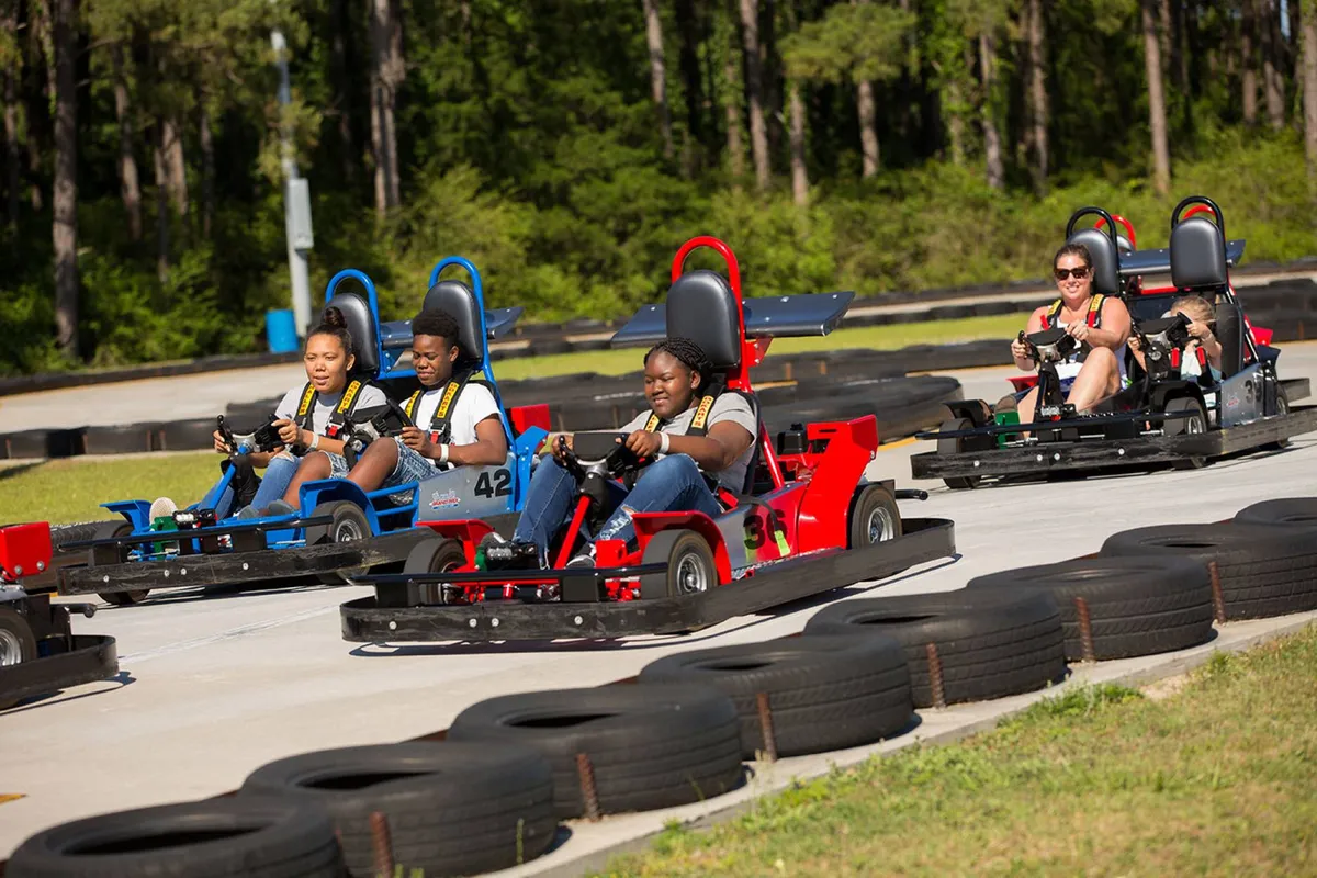 An outdoor go-kart track bustling with participants as they race around sharp turns. Families and friends are visible, engaged in thrilling, competitive fun, creating an atmosphere of excitement and togetherness.