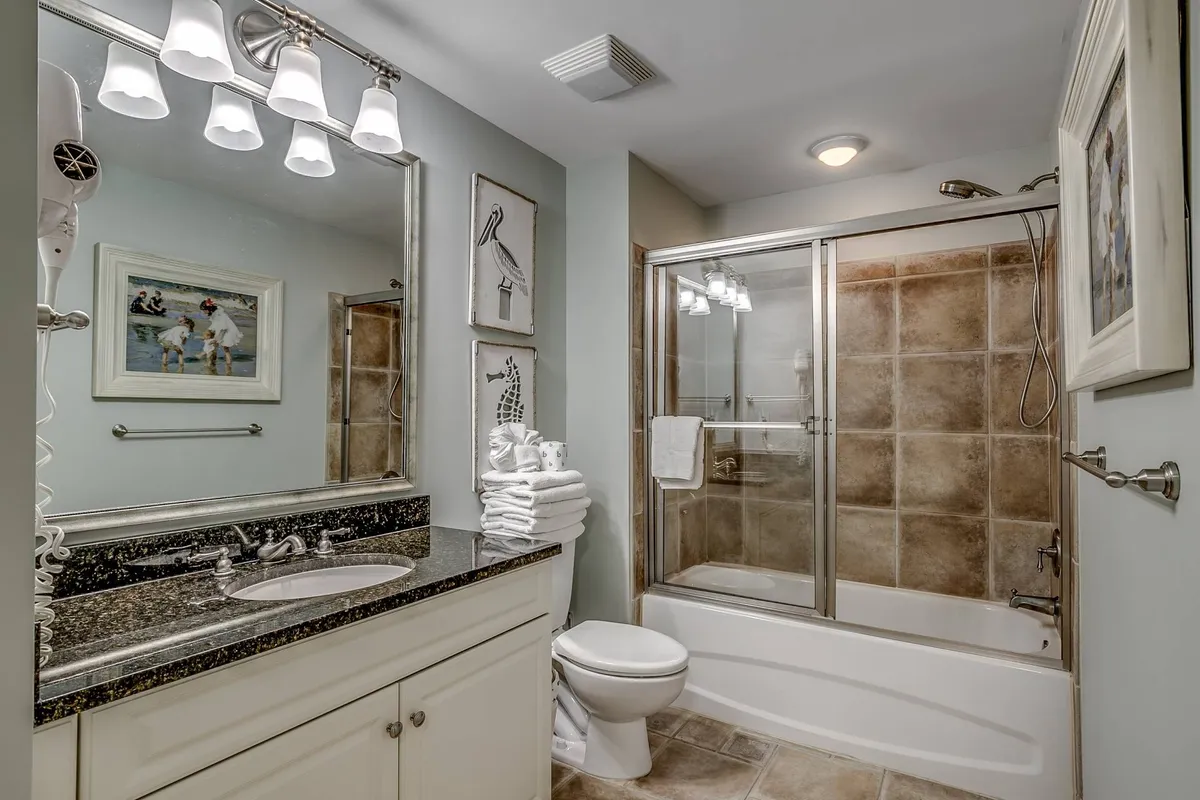 This image captures an inviting and serene bathroom interior, featuring a well-lit vanity with a large mirror, modern sink, glass shower enclosure, plush towels, and tasteful artwork. The space exudes a calming retreat ambiance.