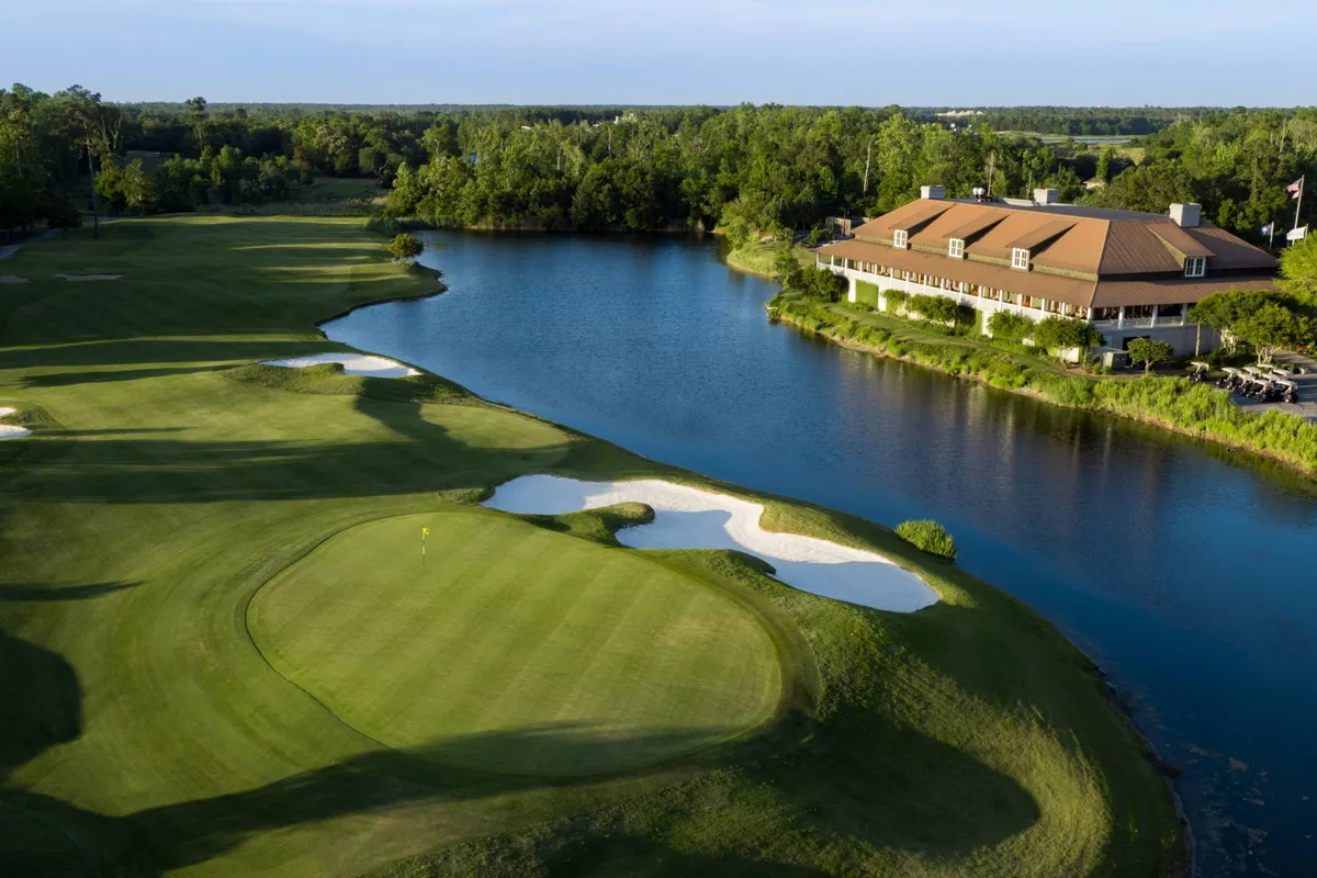 A picturesque exterior view of a lush golf course, with a water body reflecting the setting sun, the inviting clubhouse in the background, and sand traps dotting the green. The scene is tranquil yet hints at the fun and challenge of a round of golf.