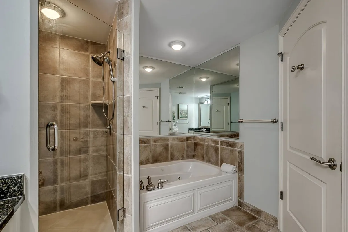A spa-like en-suite bathroom featuring a modern shower area, bathtub, and mirrored wall. The setting is tranquil and designed for relaxation and self-care routines.