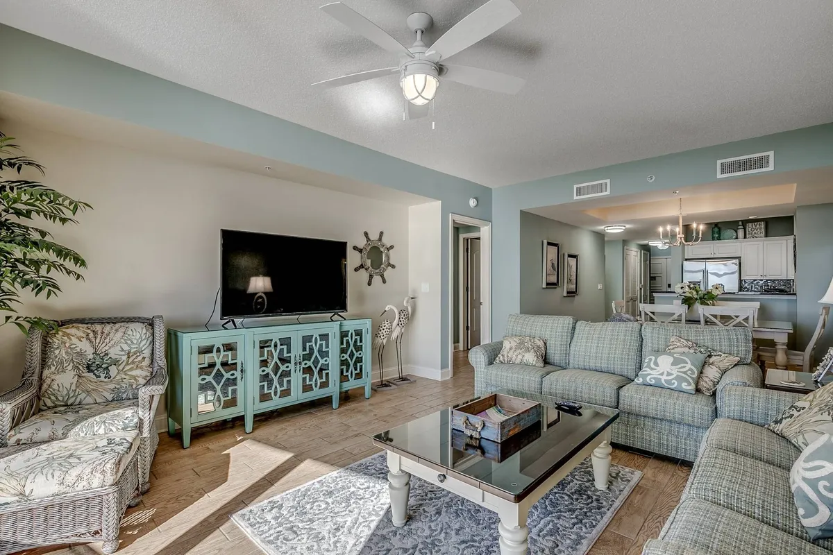 A bright, open living room featuring a plush sofa, armchair, coffee table, and television. Soft natural light fills the space, and tasteful decor adds a welcoming touch, making it ideal for relaxing or socializing with family and friends.
