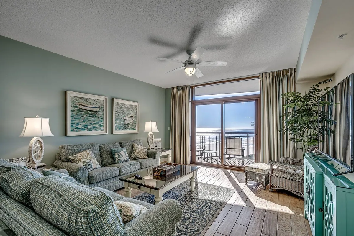 The image showcases a spacious and comfortable living area with plush seating, a coffee table, vibrant artwork, and a large window that frames sweeping views, allowing natural light to flood the space. A decorative plant adds a touch of greenery, and the layout invites relaxation, socializing, or quiet moments enjoying the scenery.