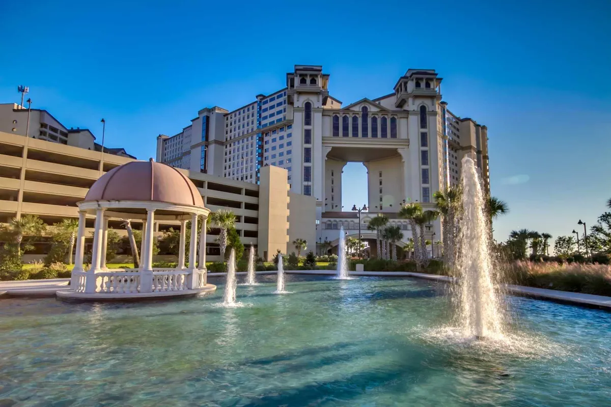 A serene exterior shot of the resort grounds highlights the elegant building architecture, a picturesque fountain, and a charming gazebo surrounded by manicured landscaping. The tranquil setting invites relaxation and hints at upscale amenities, such as outdoor gathering spots and beautiful sunset views.